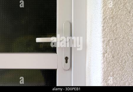 Sleek white door handle mounted on a textured metal-and-glass surface, featuring a secure lock mechanism. Stock Photo