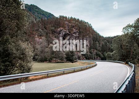 A paved road along which there are cliffs covered with forest. Stock Photo