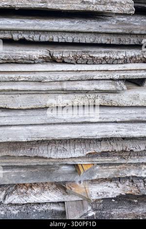 Stack of rough, seasoned wooden planks. The gray, cracked surface shows the natural texture of wood exposed to the elements. Stock Photo