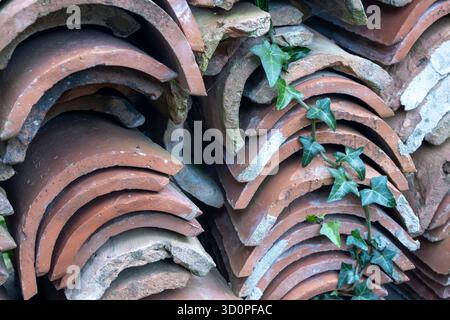 Stack of old, curved terracotta roof tiles (coppo or tegola) piled outdoors, showing wear and natural texture. Stock Photo