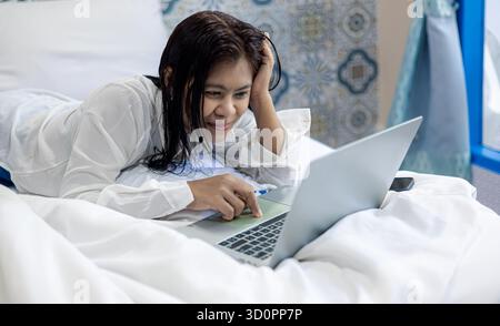 Young woman lying on bed using laptop, concept of work from home, online communication, digital lifestyle, and modern technology at home. Stock Photo