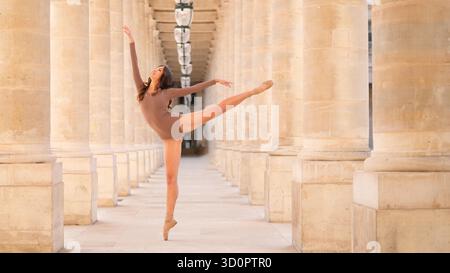 A female ballet dancer performs a perfect arabesque en pointe in a sunlit colonnade, where classical architecture meets expressive movement. || Model released Stock Photo