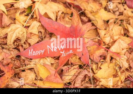 Happy New Year written on red maple leaf – autumn seasonal greeting concept. Artistic photo of a red maple leaf with the text Happy New Year written Stock Photo