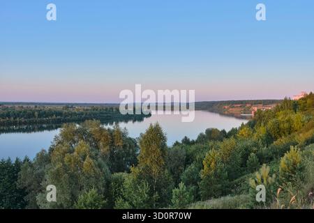 High-angle, panoramic view of wide,calm river winding through lush green valley at twilight or civil dawn. Water beautifully reflects soft gradient of Stock Photo