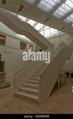 A modern interior featuring a split white staircase, translucent ceiling panels, and minimalist design. Stock Photo