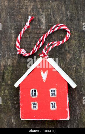 Wooden toy house on a wooden surface with a twisted string, the house is red and the roof is white and there are four windows on the house. Stock Photo