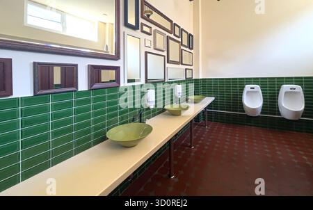 Modern public men's restroom featuring green tiled walls, multiple sinks, and a collage of mirrors Stock Photo