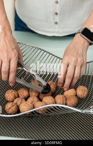 Woman's hands extracting walnuts from a metal basket, preparing to crack them Stock Photo