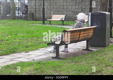 A lonely man sits on a bench in a park in cloudy weather Stock Photo