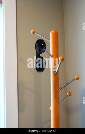 Sunglasses hanging on a freestanding clothes rack or entry hall tree in the corner by a window. Stock Photo