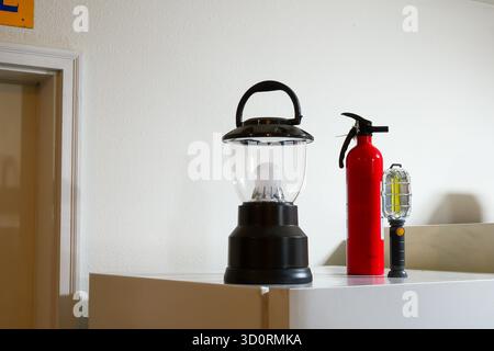 A black battery powered lantern sits on top of refrigerator, near another light and a fire extinguisher. Stock Photo