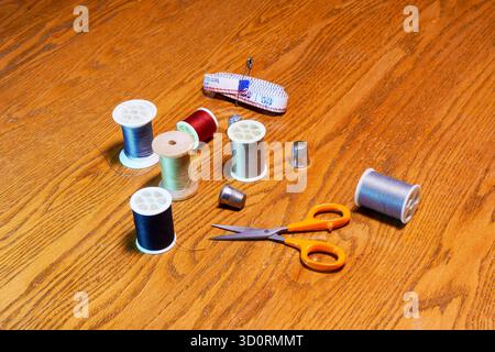 Spools of colored thread, thimbles, scissors and a tape measure on a wooden surface. Stock Photo