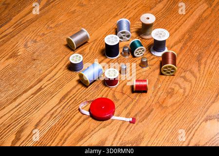 Spools of colored thread, thimbles, and a retractable tape measure on a wooden surface. Stock Photo