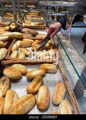 A hand is reaching for fresh bread rolls in a bakery display case, surrounded by an assortment of baked goods, highlighting the atmosphere and texture Stock Photo