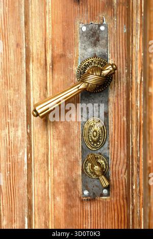Nahaufnahme einer hölzernen Tür mit kunstvoll verzierter Messingklinke in Knotenform Stock Photo