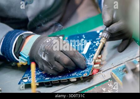 Skilled technician performing soldering on a circuit board in a modern electronics workshop during the daytime Stock Photo