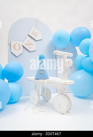 Blue balloons, wooden ONE banner, and small tricycle create soft pastel first birthday setup, perfect for boys milestone celebration Stock Photo
