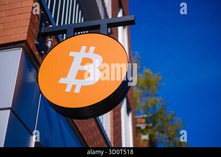 Shop sign featuring the Bitcoin cryptocurrency logo, with a vibrant blue sky in the background Stock Photo