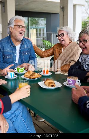 Happy group senior people laughing and enjoying coffee sitting at cafeteria bar table for breakfast Stock Photo