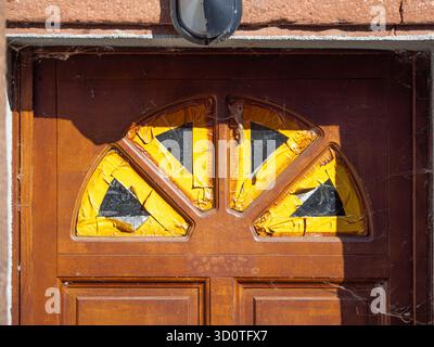 Wooden door with broken glass panes covered by yellow tape. Stock Photo