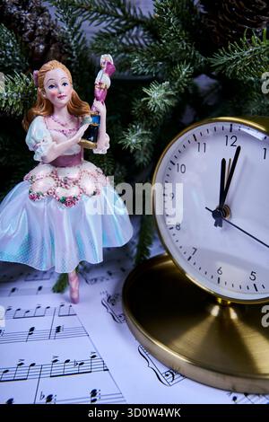 Christmas still life with Nutcracker‑style figurine, brass clock near midnight and sheet music beneath evergreen branches and frosted pinecones Stock Photo