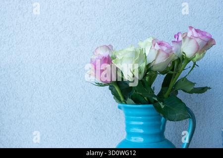 Pink and white roses in turquoise ceramic vase against light blue wall, romantic floral home decor Stock Photo