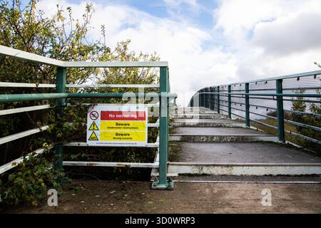Warning sign reading “No swimming, Beware underwater obstructions, Strong currents” beside a green footbridge near Gunpowder Park, Enfield. Stock Photo