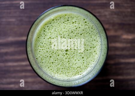 Glass of green smoothie, close up, top view. Healthy organic drink made from banana, dill, parsley and avocado. Bubbles and foam on the surface of a g Stock Photo