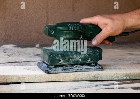 Worker sands wooden boards using a vibration sander in a workshop, close up. Power tool Stock Photo