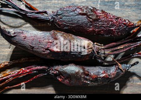 Three baked young beets in skins on a wooden cutting board, close up, top view. Organic vegetables, healthy vegan eating, harvest time Stock Photo