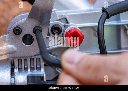 A man unscrews the bolt with a hex wrench for adjusting the miter saw, close up. Worker with allen screw with his wrench Stock Photo