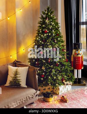 Christmas tree is lit up with lights and ornaments. A nutcracker is standing next to the tree Stock Photo