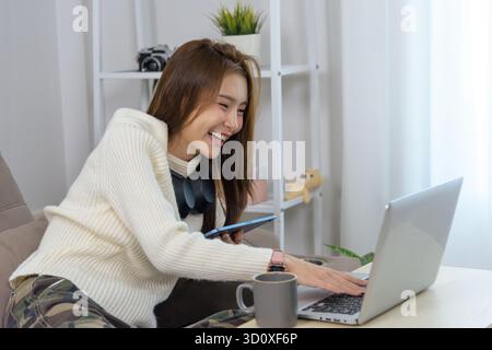Young happy woman engages in home activity, people connect using laptop, smartphone, enjoying remote work, online learning, or entertainment, smiling Stock Photo