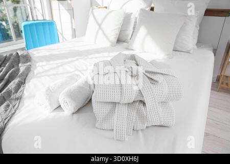 Folded bathrobes with towels on bed in hotel room Stock Photo