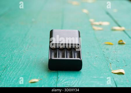 A battery charger is placed on a weathered green wooden table, surrounded by scattered yellow and brown leaves, showcasing autumn vibes. Stock Photo