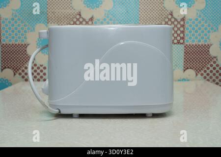 A white toaster sits on a light kitchen counter, featuring a colorful patterned backdrop of dots and flowers. Stock Photo
