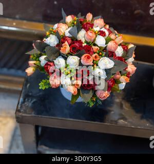 A bright and dense arrangement of artificial flowers in shades of red, white, and coral sits on a dark, rustic surface. Stock Photo