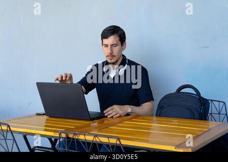 Man focusing on his laptop, working or studying from a cafe table with headphones around his neck, displaying modern work concepts Stock Photo