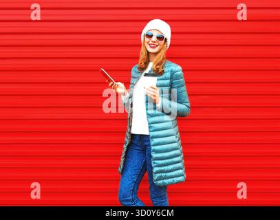 Fashion smiling woman holds smartphone, coffee cup on a red background || Model released Stock Photo