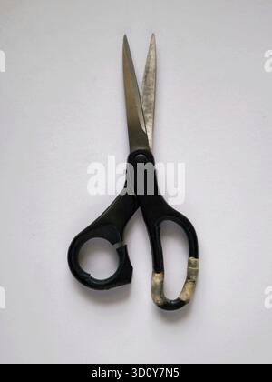A pair of scissors with a broken black handle that looks like it has been repaired and a blade that is also full of signs of use on a white background Stock Photo