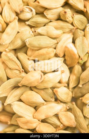 A vibrant, vertical close-up, full-frame background of numerous dried green cardamom pods (Elettaria cardamomum). The image showcases the delicate tex Stock Photo