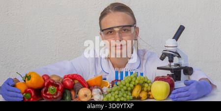 Female scientist in safety glasses and gloves examining fresh fruits and vegetables. Stock Photo
