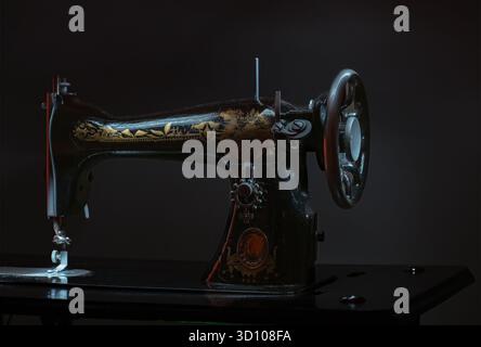 A vintage sewing machine with gold and black embroidery. The machine is turned off and is sitting on a table Stock Photo