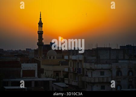 A mosque and minaret silhouetted against a setting sun at golden hour over the city of Cairo, Egypt. Stock Photo