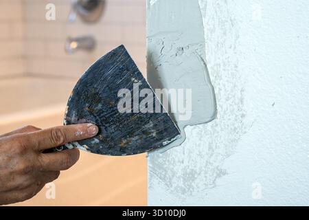 A joint knife flattens putty compound on an interior drywall surface during mudding to prepare for painting during renovation. Stock Photo