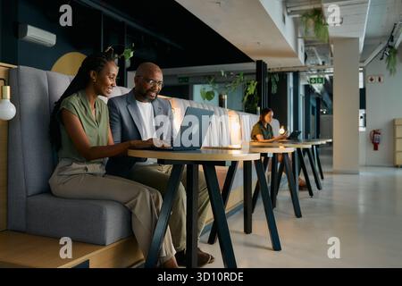 Happy black businessman and businesswoman working on laptop sitting at desk in office lounge Stock Photo
