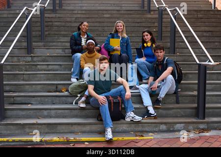Diverse students sitting on campus stairs looking at camera Stock Photo