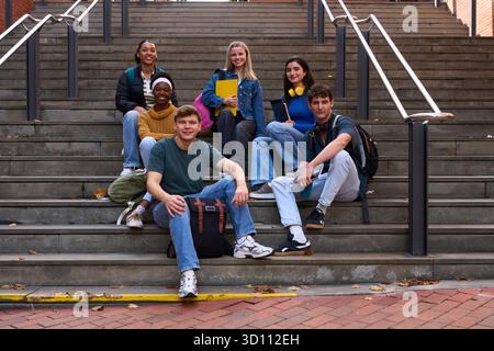 Diverse students sitting on campus stairs looking at camera Stock Photo