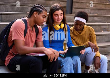 Diverse students collaborating on tablet at university stairs Stock Photo