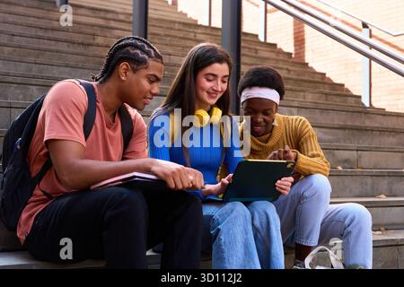 Diverse students learning together on tablet on campus stairs Stock Photo